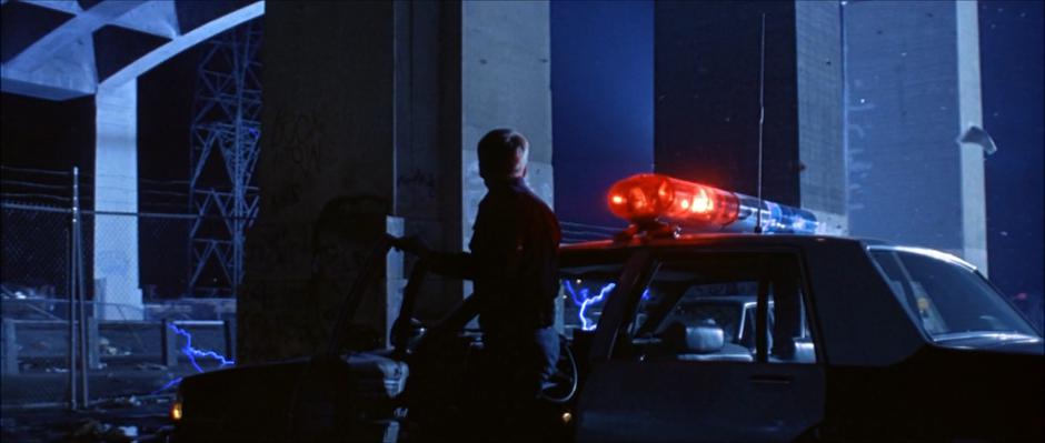 A police officer gets out of his car as lightning continues to spark under the bridge.