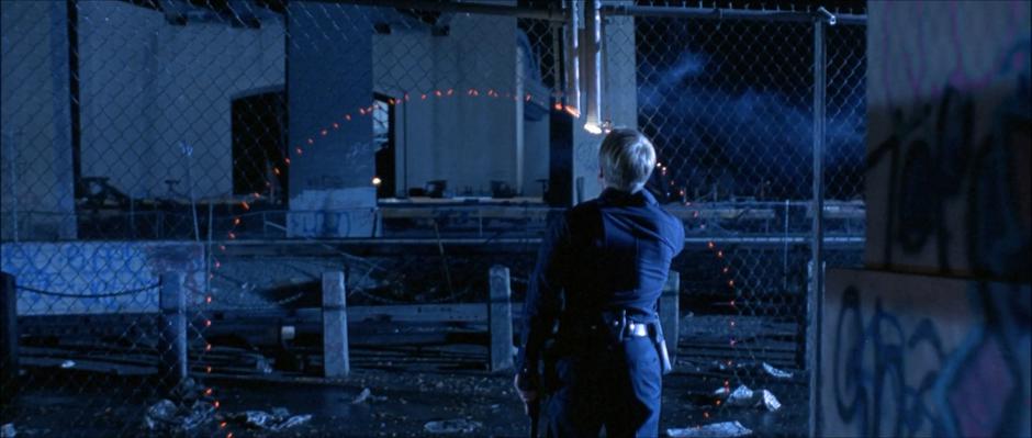 A police officer shines his flashlight on the circular hole burned into the fence.