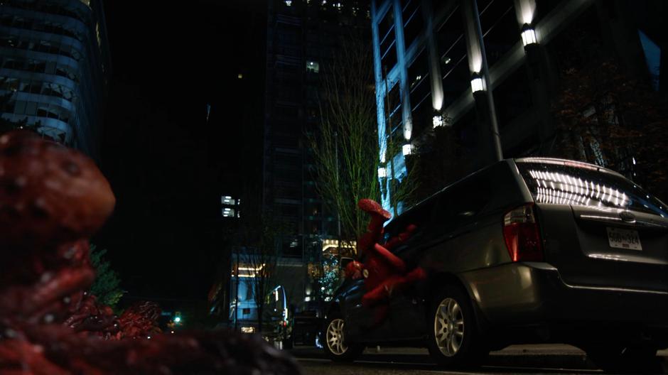 The giant monster form of Ramsey throws Barry into a parked car.