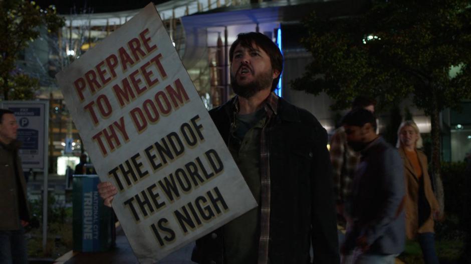 A man with a sign prophesying the end of the world stands on the street yelling.