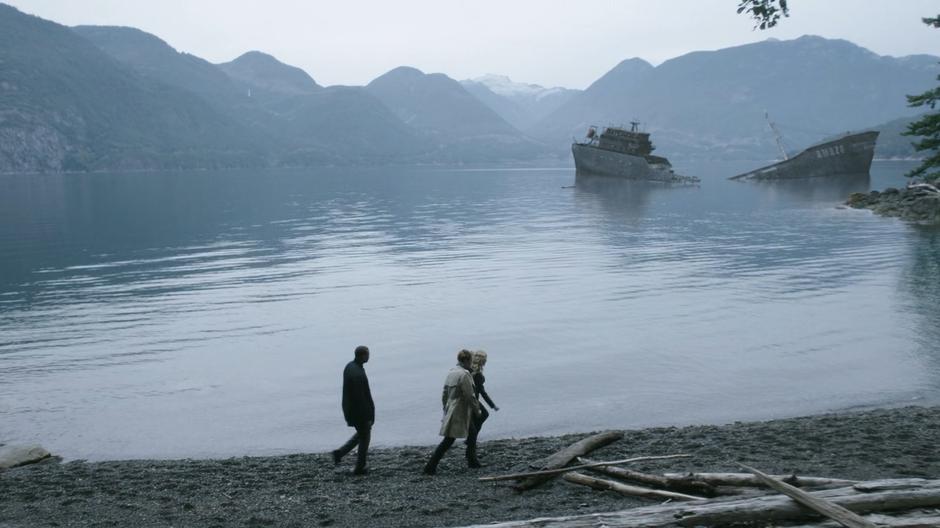 Diggle, Constantine, and Mia walk along the shore with the shipwreck in the background.
