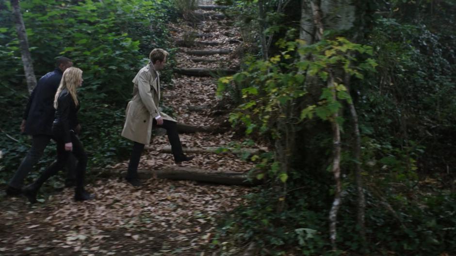 Diggle, Mia, and Constantine walk through the forest past some stairs in their search.