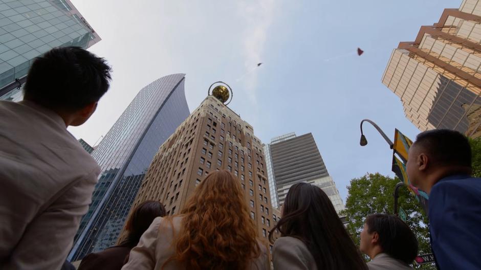 People on the street look up to see the two Supermen fighting in the sky.