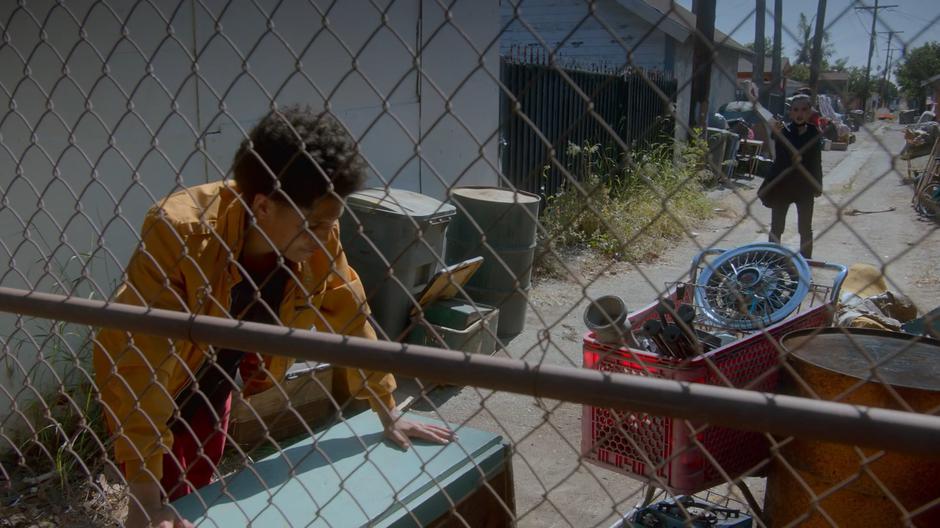 The Son stops moving a desk to climb over the fence when Nico comes up on him with Tamar's gun raised.