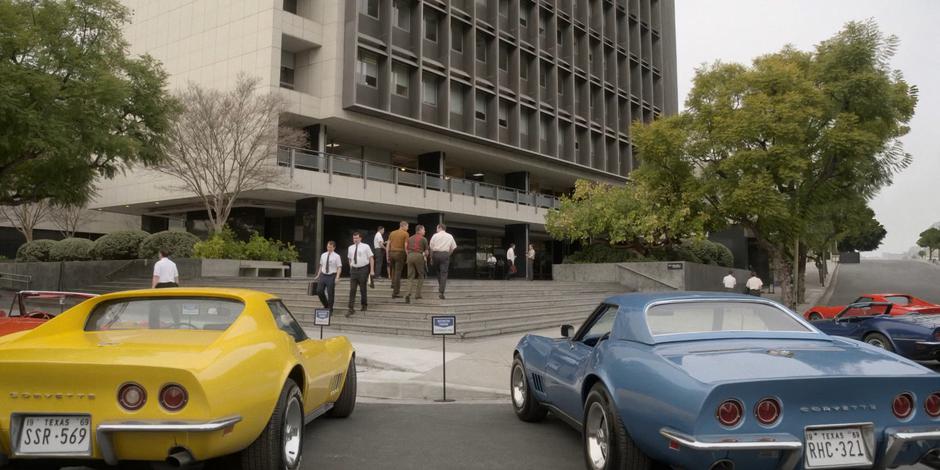 A group of astronauts walk up the steps to the building from their parked Corvettes.