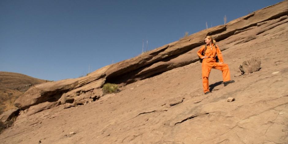 Tracy glances around while standing on a rock slope.