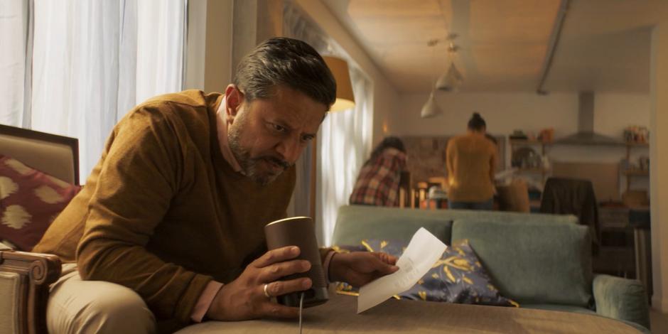 Hakim tries to get his voice assistant to work while his family chats in the kitchen behind him.