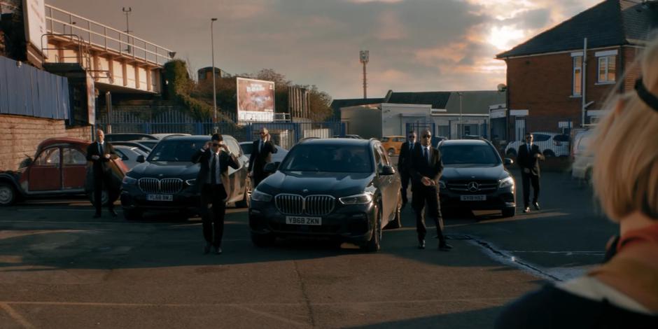 Several government agents stand by their car as one walks over towards the Doctor.