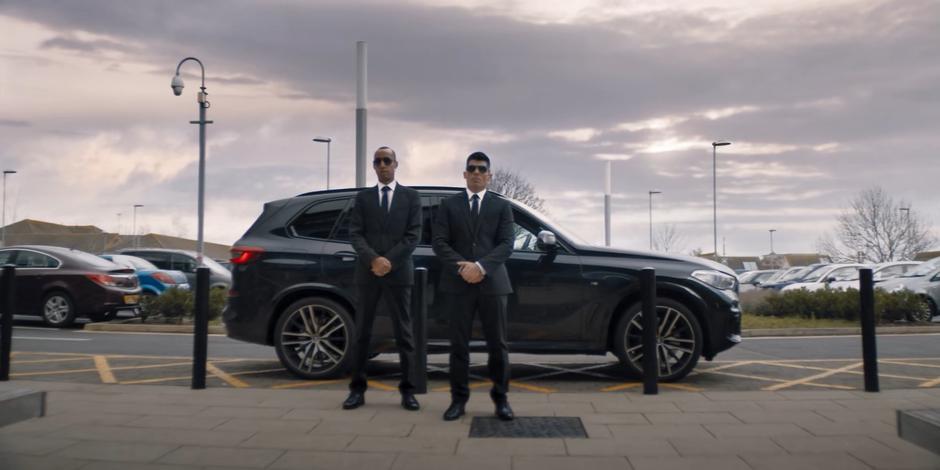 Two government agents stand by their car waiting for Graham.