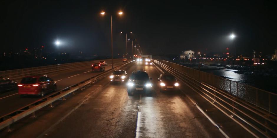 The government vehicle accelerates backwards through traffic across the bridge.