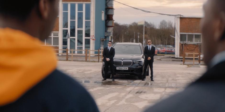 Two government agents stand by their car waiting for Ryan.