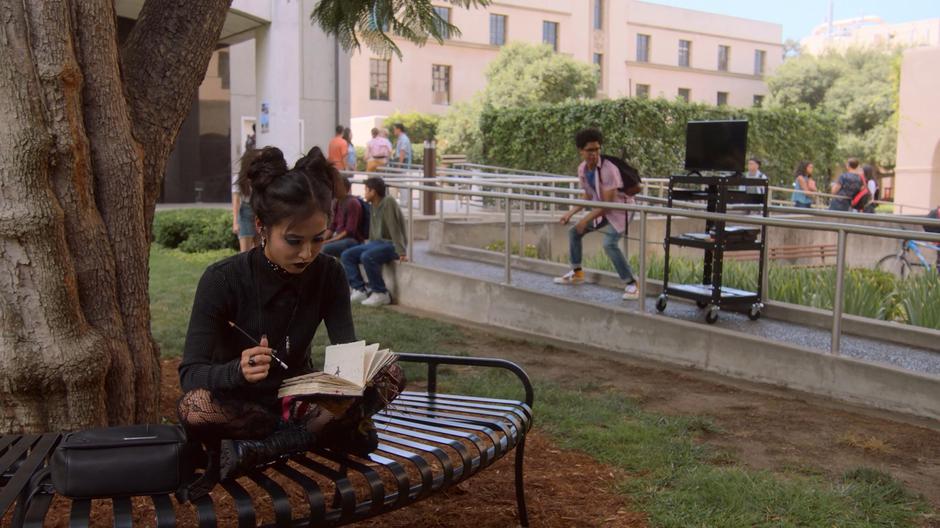 Past Nico writes in her notebook while behind her past Alex struggles with the AV cart.