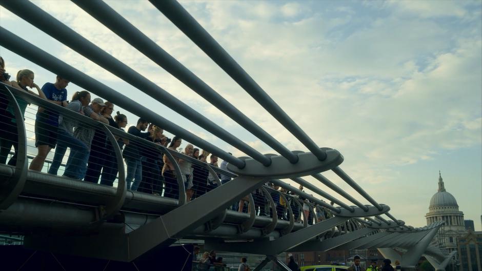 Bystanders line up along the edge of the bridge looking down at the crime scene.