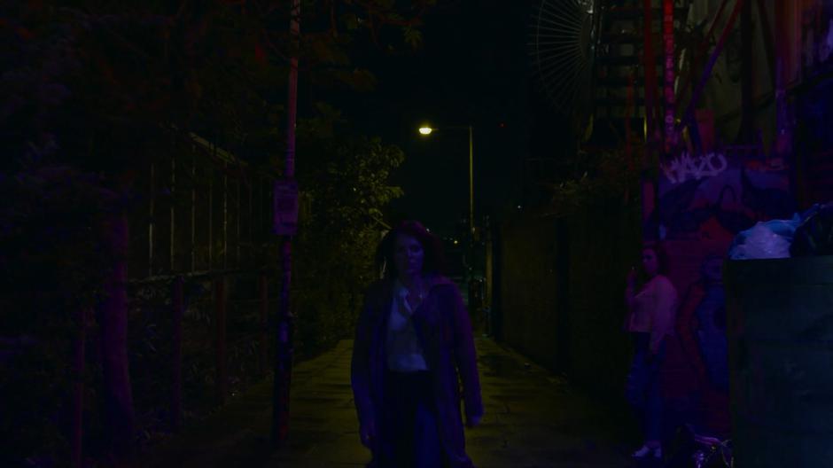 Myfanwy walks down the dark alley towards the street.