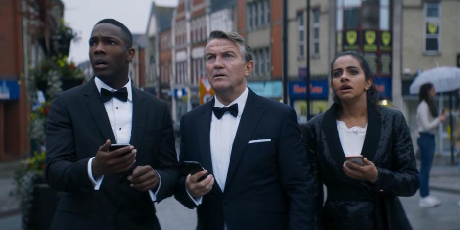 Ryan, Graham, and Yaz look up at the screen as they listen to Daniel Barton over their phones.