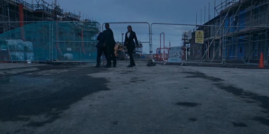 Ryan and Yaz check behind them as Graham unlocks the gate leading to the construction site.