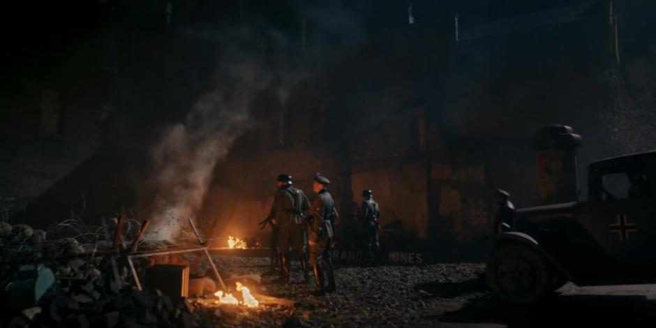 Several Nazi soldiers exit their vehicles and spread out on the rubble-strewn street.