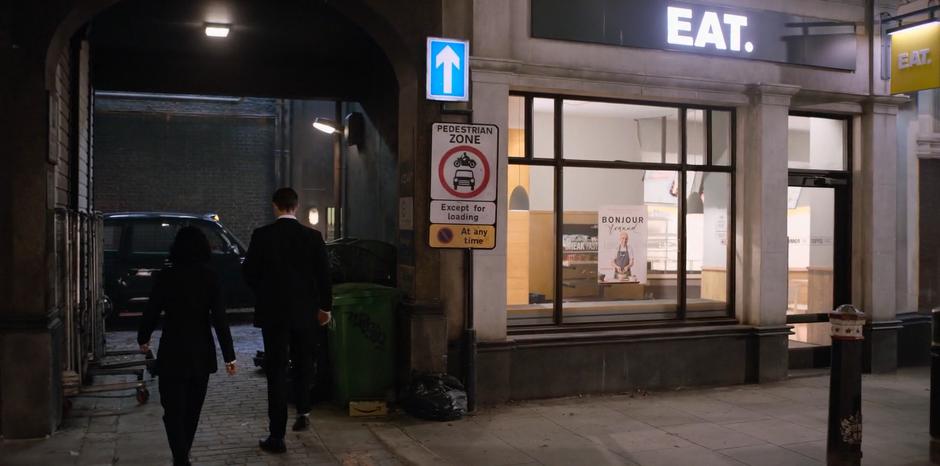 H leads M into a side alley where a Black Cab is waiting.