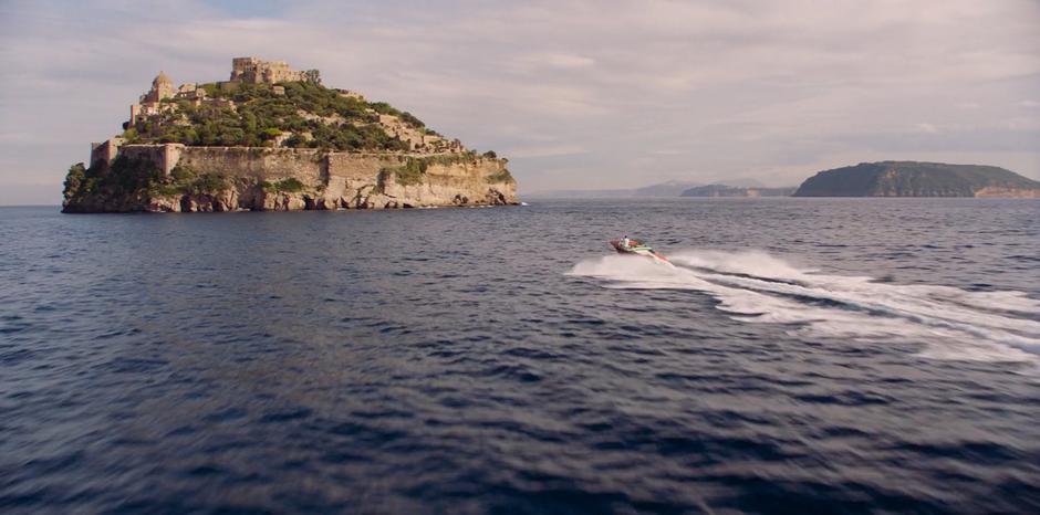 H pilots his speedboat towards the island fortress.