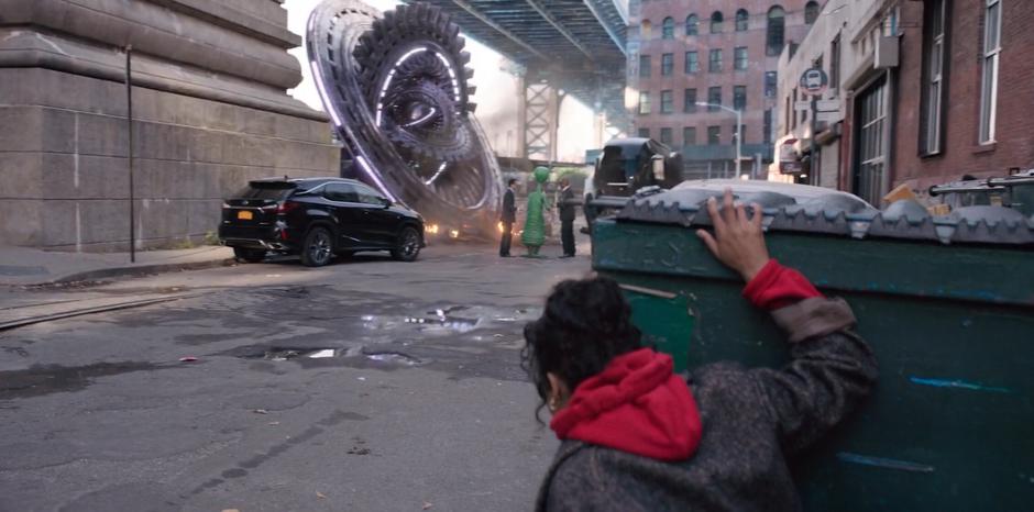 Molly crouches behind a dumpster after walking through the hologram and sees two M.I.B. agents talking to the alien Jimmy in front of his crashed spaceship.