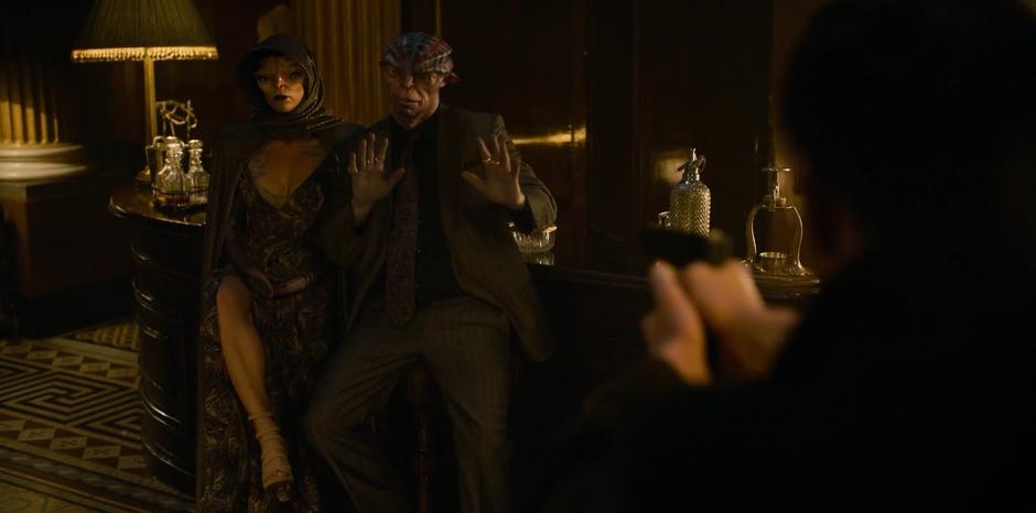 The alien boss raises his hands while H points his gun at him and his wife.