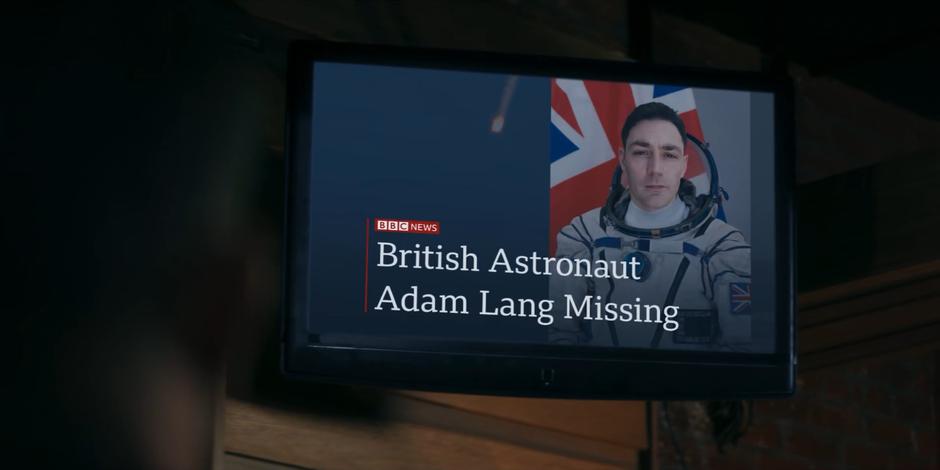 The TV in the corner of bar displays a news report on Adam Lang's disappearance after the crash.
