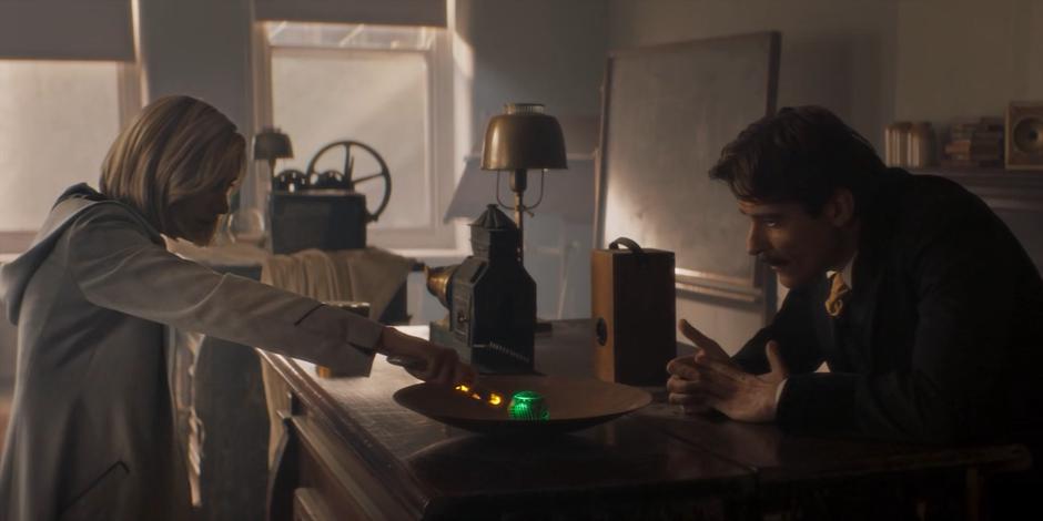 Nikola Tesla leans over the table as the Doctor scans the ball with her sonic.