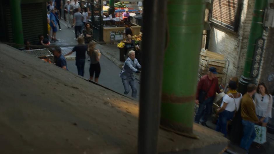 Monica and Gestalt push their way through the crowd while running across the market.