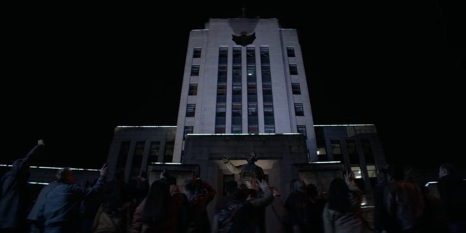 The protestors cheer as Kate jumps from the roof of the police headquarters with her Batwoman cape spread side.