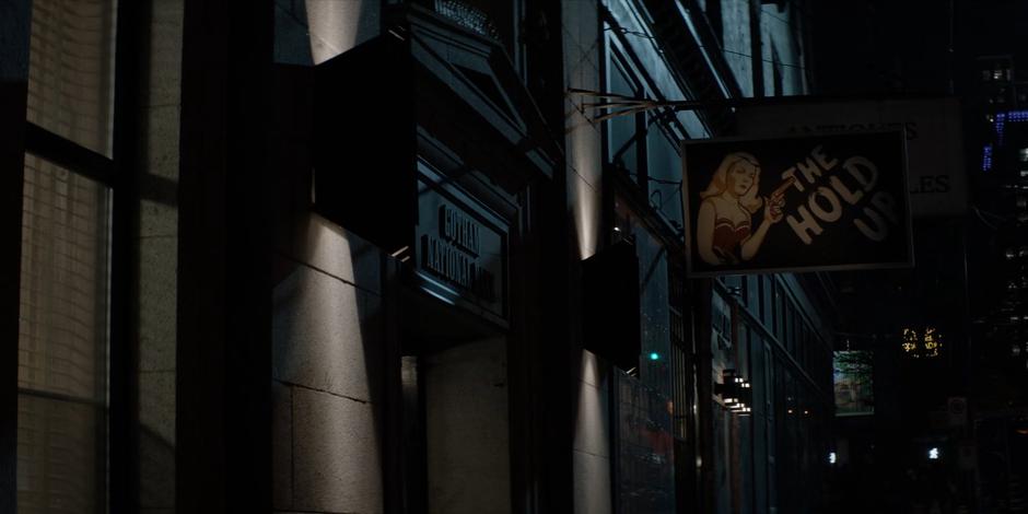 Establishing shot of the bar with its old Gotham National Bank sign and new The Hold Up sign.