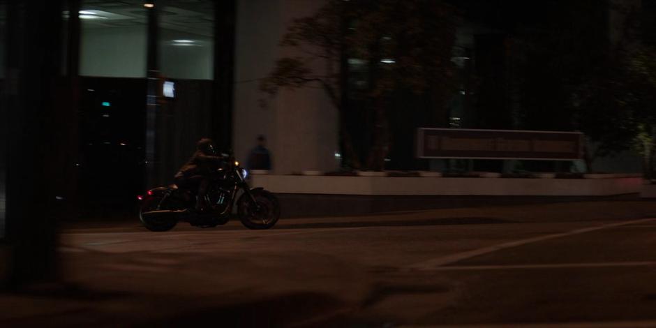 Kate drives her motorcycle through an intersection at night.