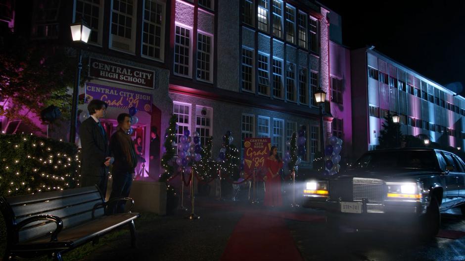 Ray and Nate stand to one side while Tiffany watches Freddy arrive in a limousine.