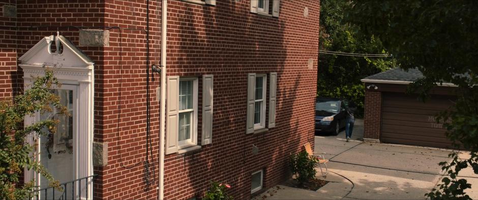 A man messes with the door of a car parked behind a building.