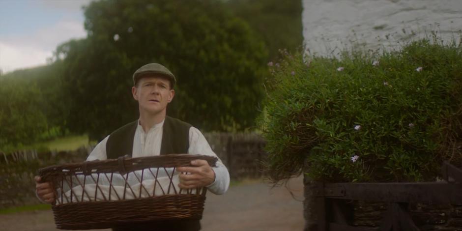 Patrick walks around the corner with the basket containing baby Brendan.