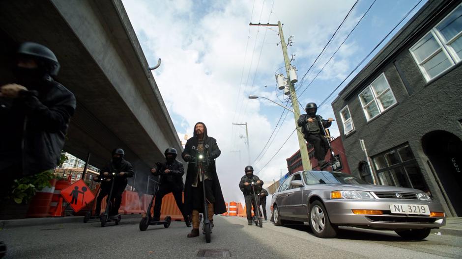 Genghis Khan and a small group of gang members ride down the street on their scooters.