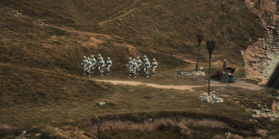 Two groups of Cybermen walk up the path from the shore.