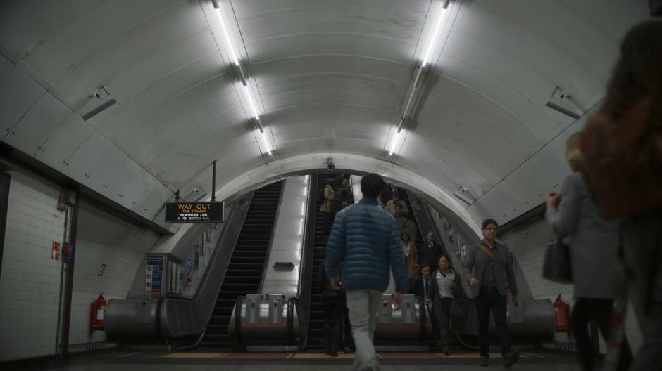 Eve steps off the escalator into the station.