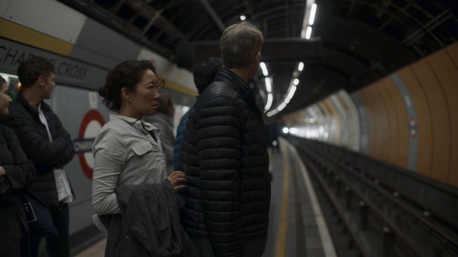 Eve stands behind the rude man and contemplates pushing him onto the tracks as the train approaches.