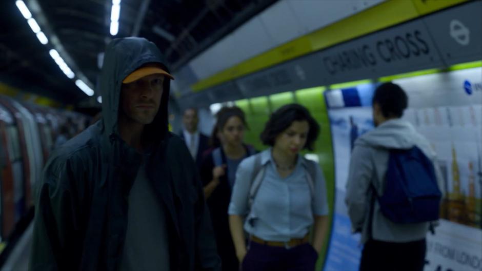 A man with his face shaded follows the figure in a hoodie out of the train.