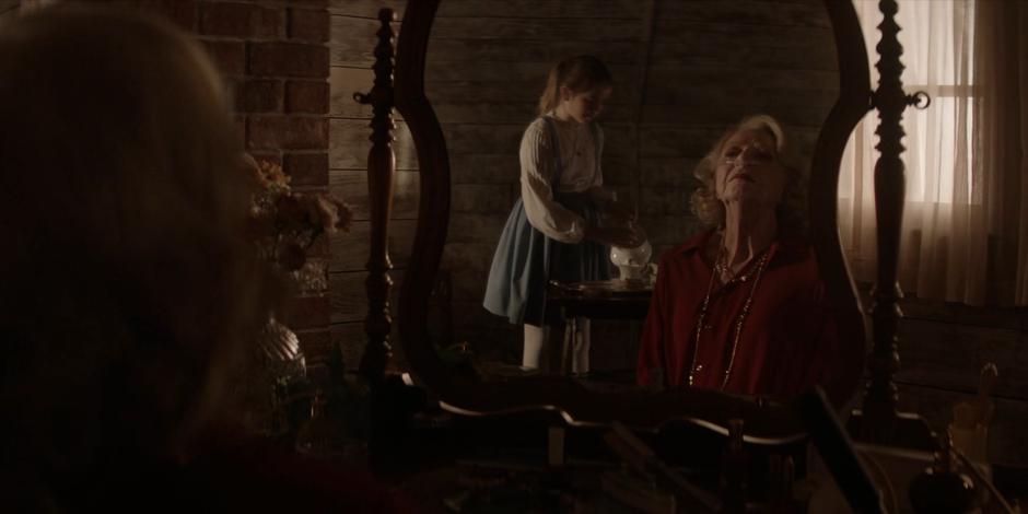 Young Alice pours tea while Mabel Cartwright examines herself in the mirror.