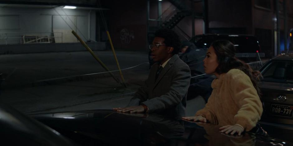 Luke and Mary watch from outside their car as Batwoman races past and takes out the guards.