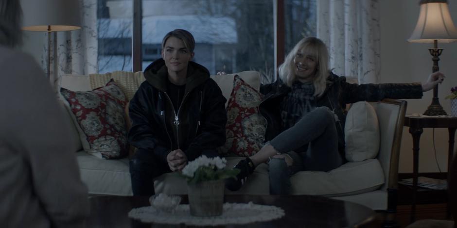 Kate sits on the couch next to Alice who is spreading her arms wide and smiling at Tammy.