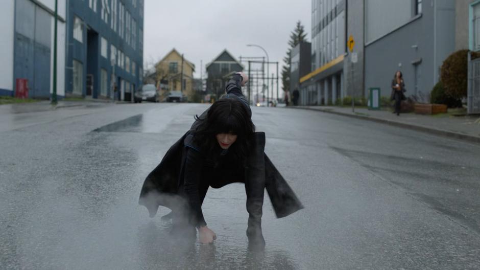 Alex does a superhero landing in the street in her black Supergirl outfit.