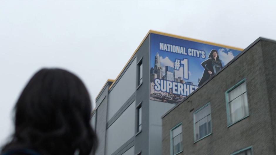 Alex looks up at a billboard calling her National City's #1 superhero.