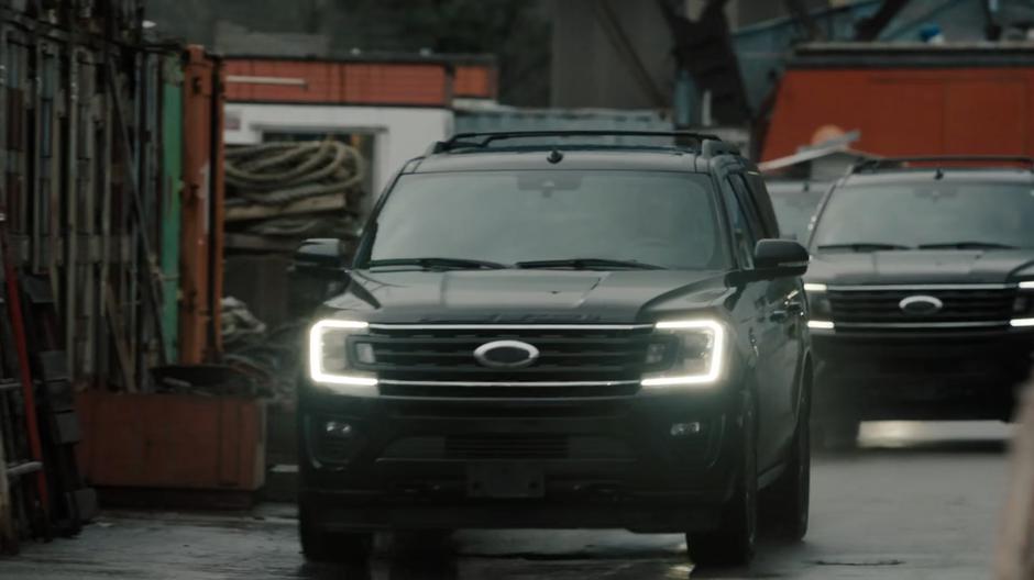 Dark SUVs drive down the dock towards the commotion.