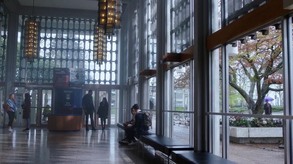 Galvin turns over his shoulder to talk to Mel as they walk through the lobby.