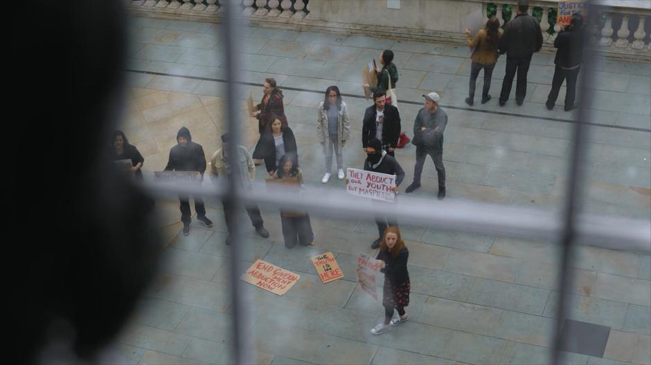 Linda looks out the office window and sees protestors down below.