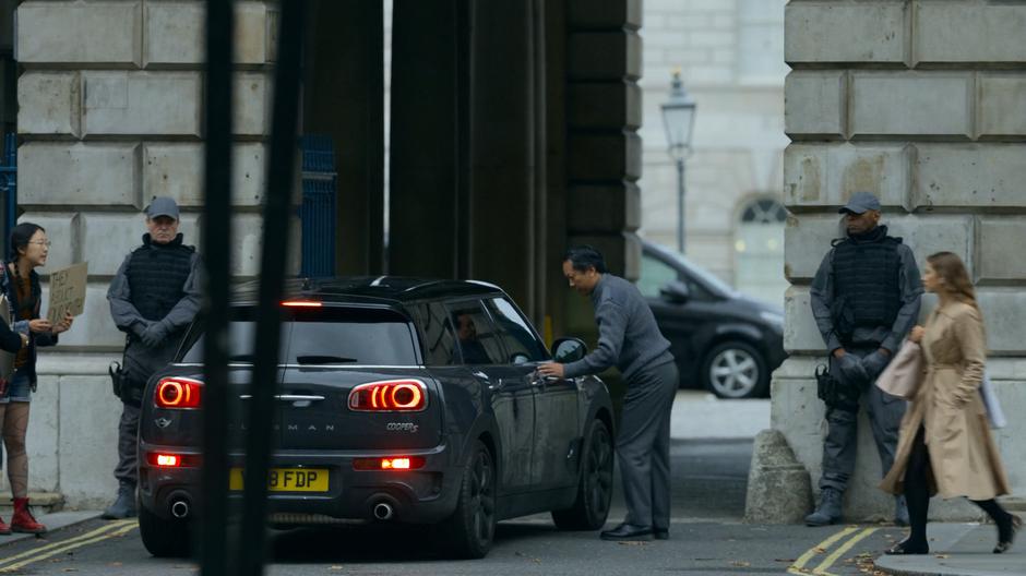 A guard leans over to check Myfanwy's car at the gate.