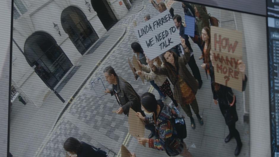 Bronwyn holds up a sign to the camera with the protestors asking to talk to Linda Farrier.