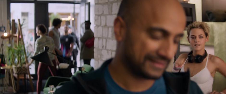 Sabina walks up behind Pradeep Prasad who is standing at the gym reception desk.